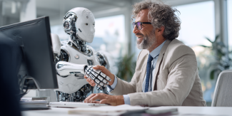 Em um escritório iluminado, um homem sorridente de terno e um robô branco apertam as mãos sobre uma mesa com um computador, mostrando interação.